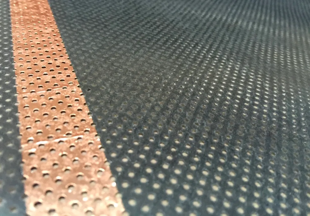 Close-up of the perforated carbon-fibre heating element with its copper bus bar