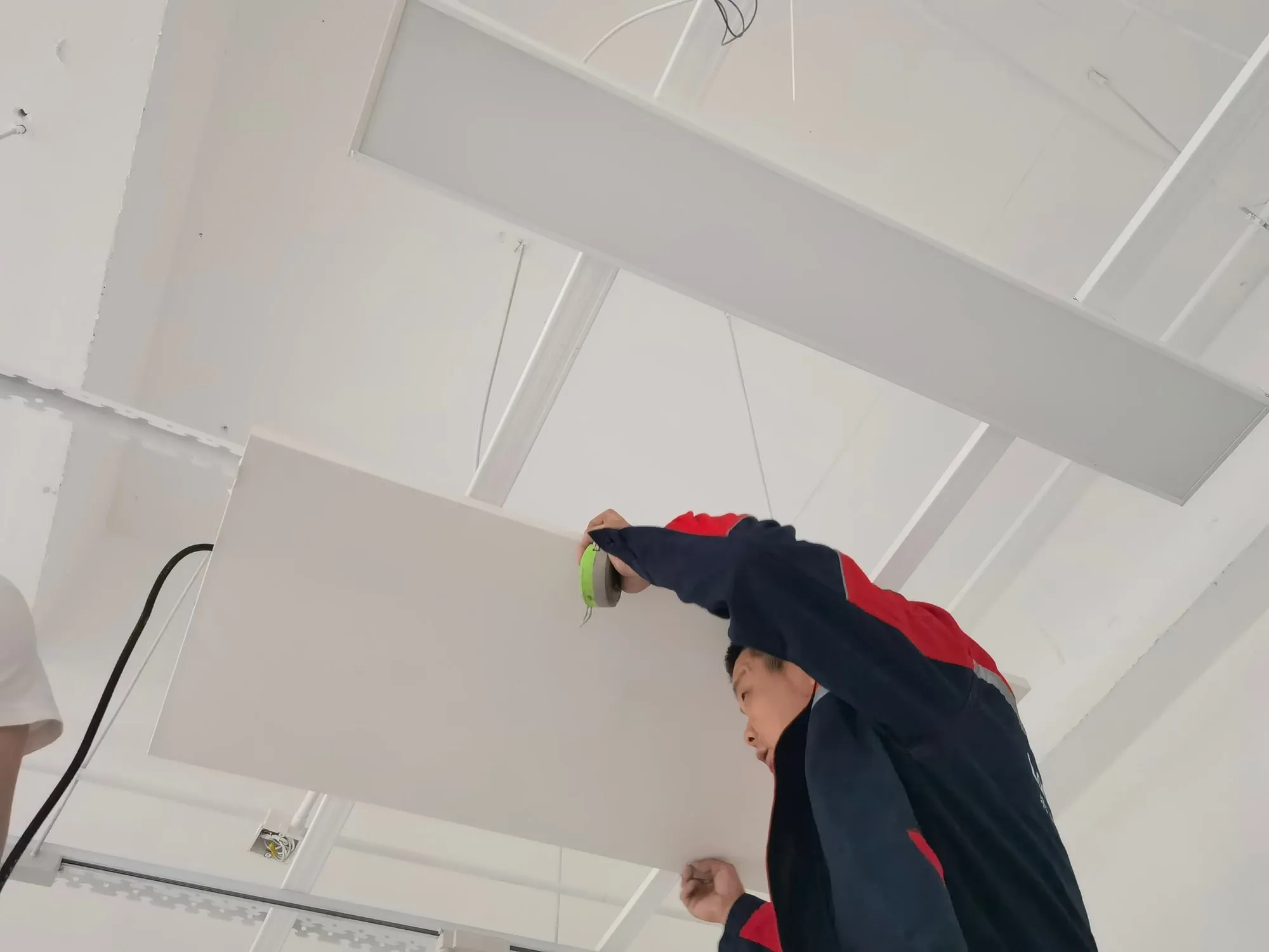 An installer sealing the edge of a mounted PowerBoard panel on the ceiling