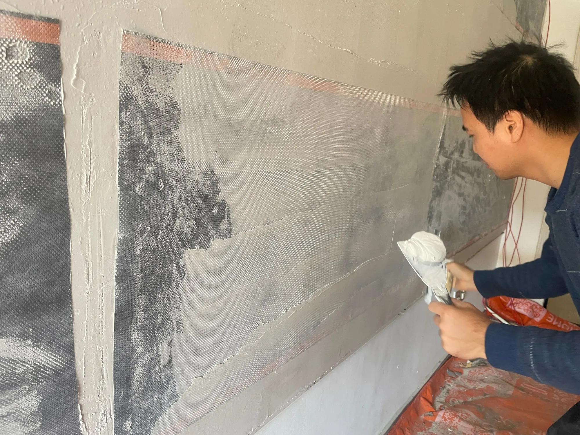 A plasterer skimming plaster over a full wall of ComfortScrim